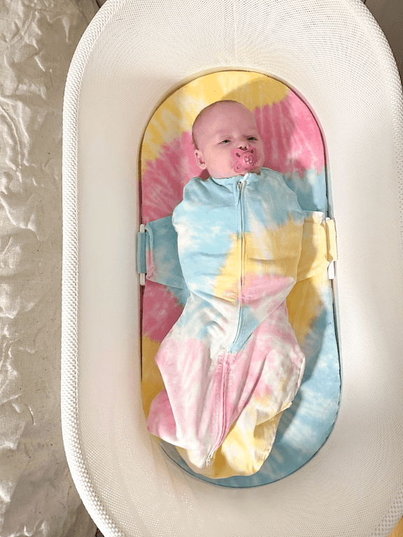 A calm baby lies in the Organic SNOO Sleep Sack in the SNOO bassinet