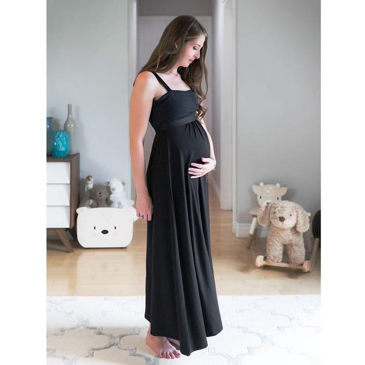 Pregnant woman standing in a room wearing a black camisole dress