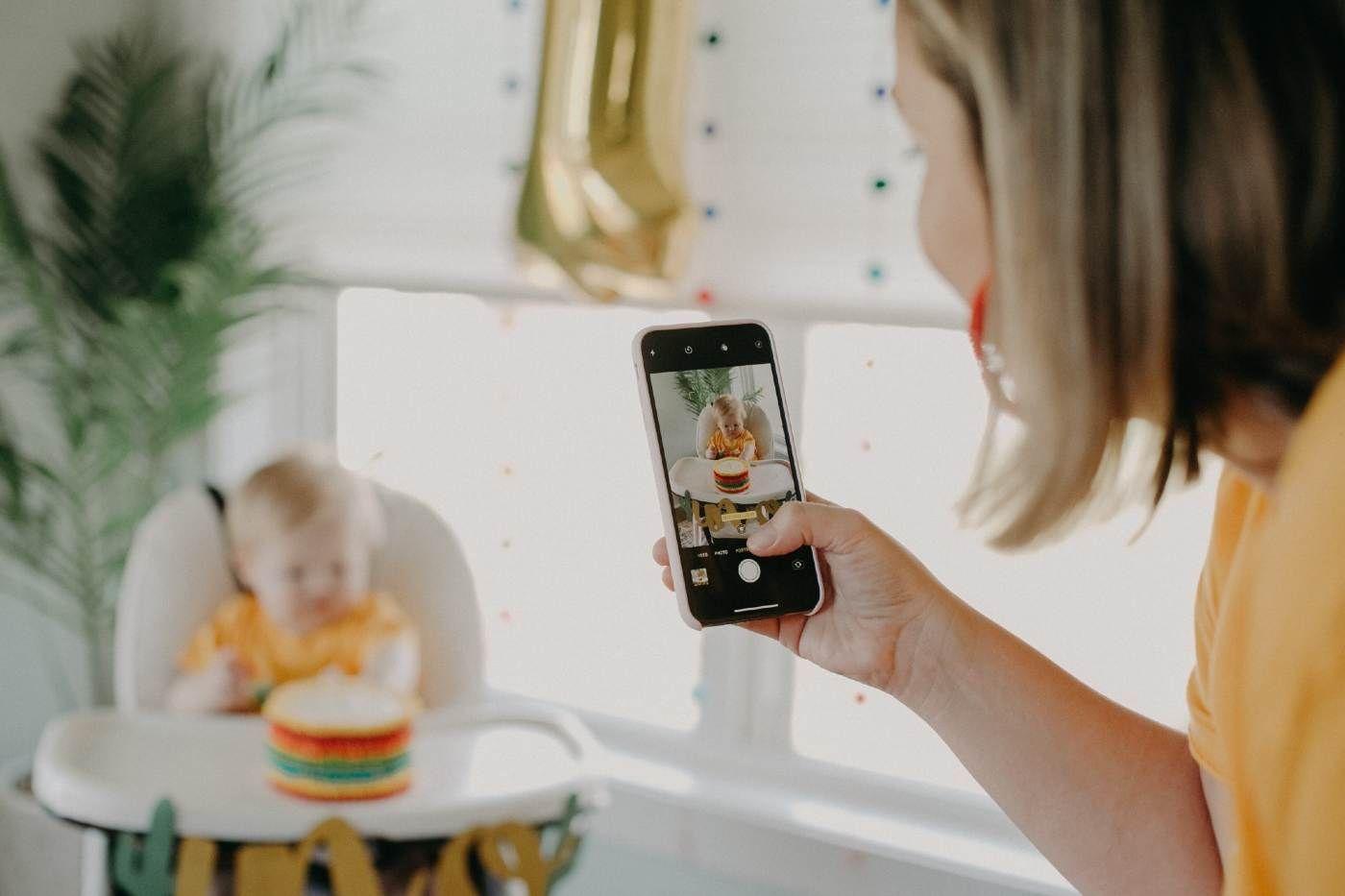 Mom uses a phone to record a video of a baby with a smash cake to celebrate a first birthday