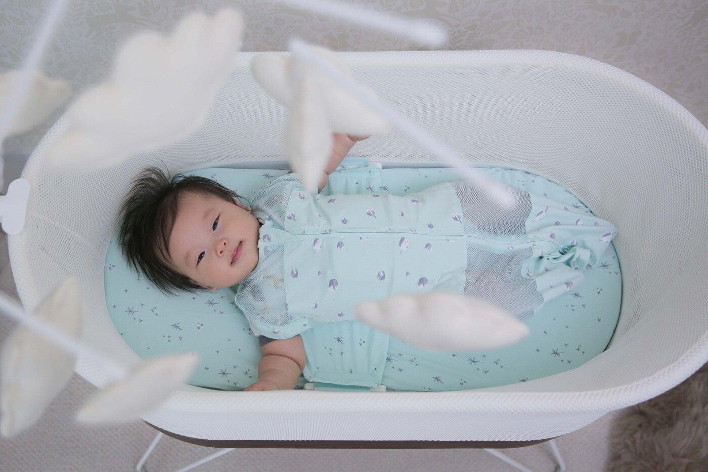 Baby gazes up from SNOO at Sky, a cloud baby mobile from Happiest Baby