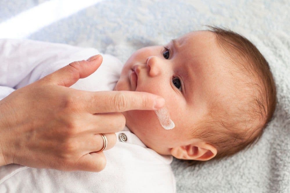 A parent applies lotion to their baby's cheek