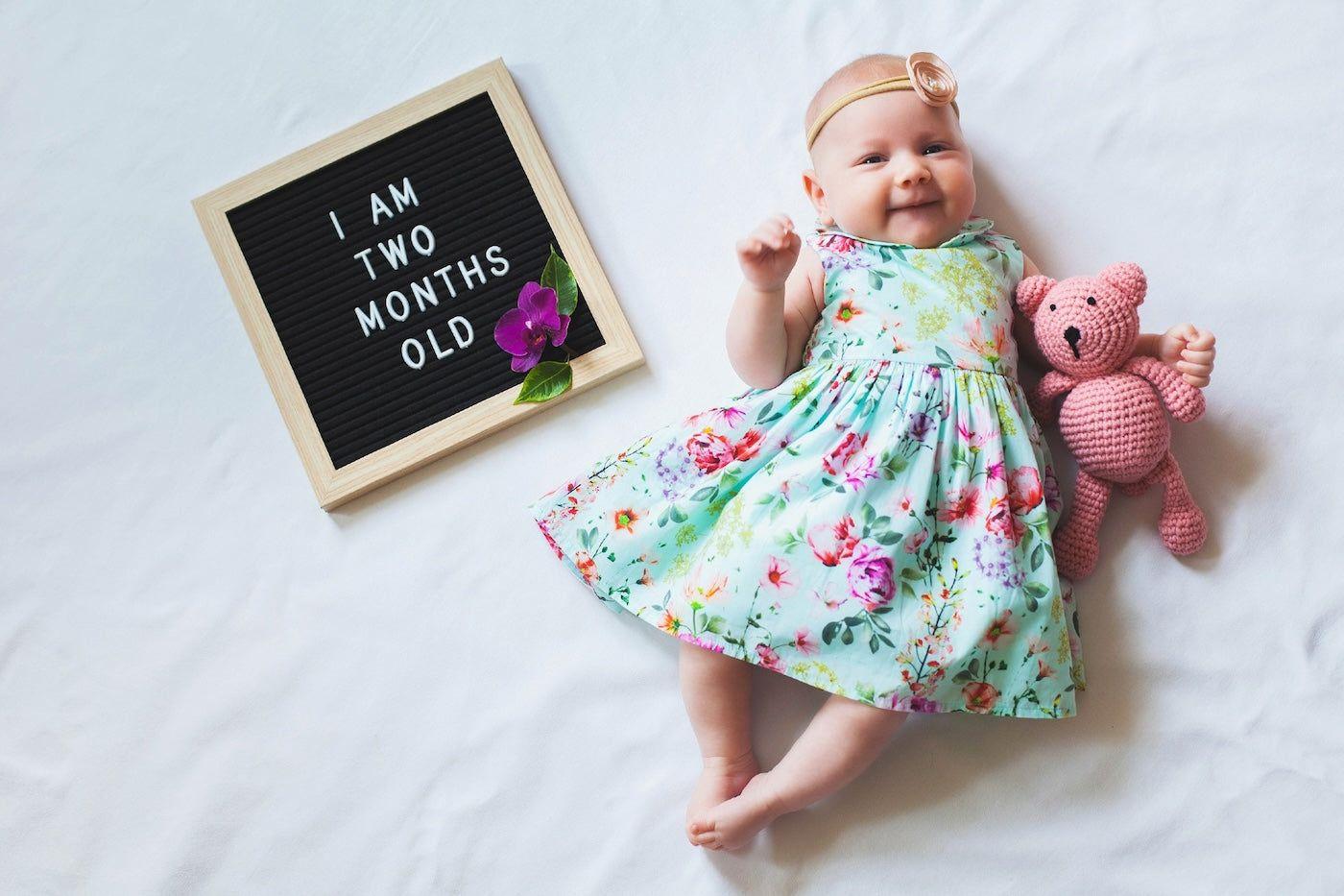 2-month-old baby girl poses with teddy bear and letterboard that says 'I am two months old"