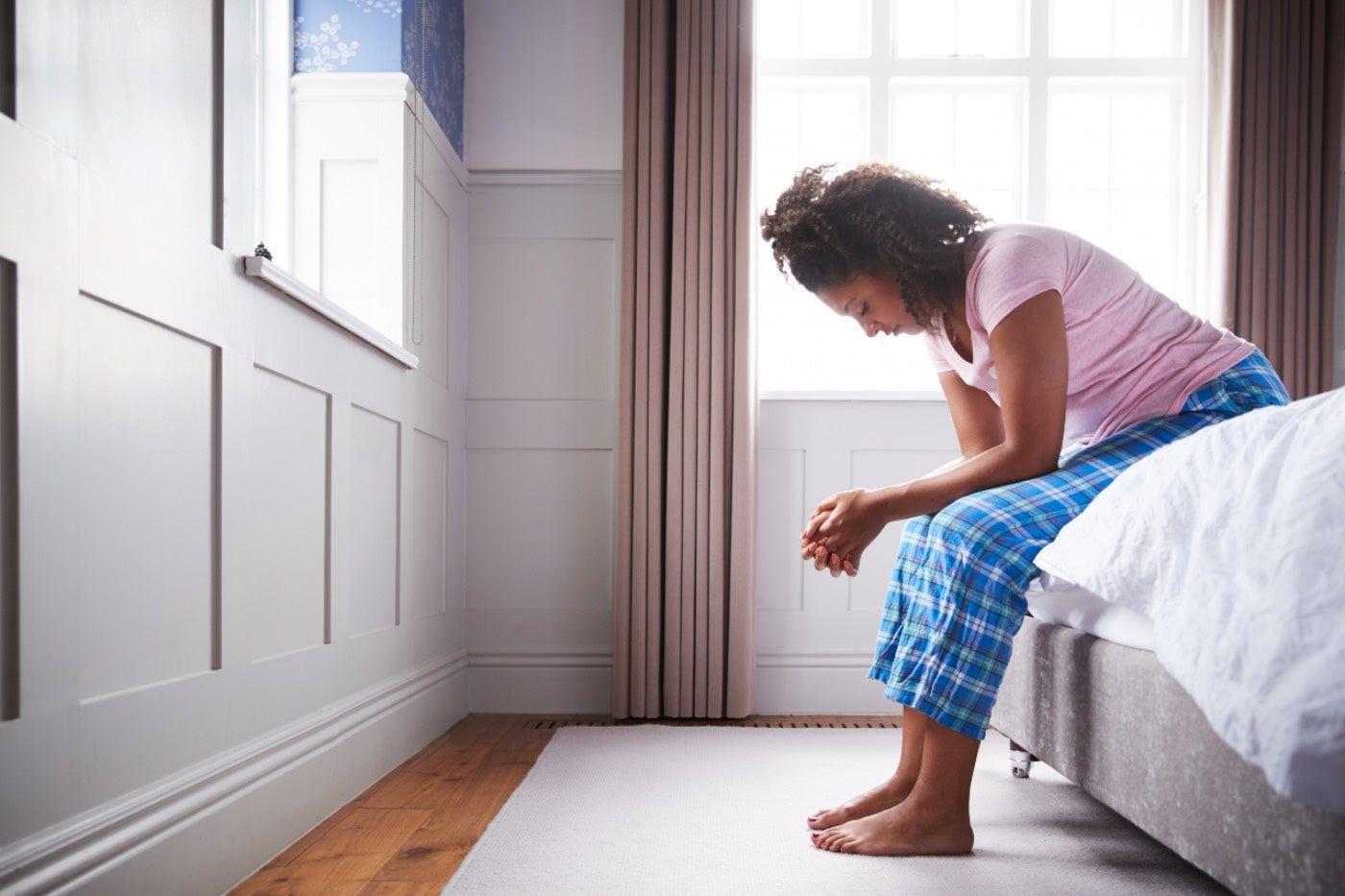 Woman sitting on bed experiencing morning sickness