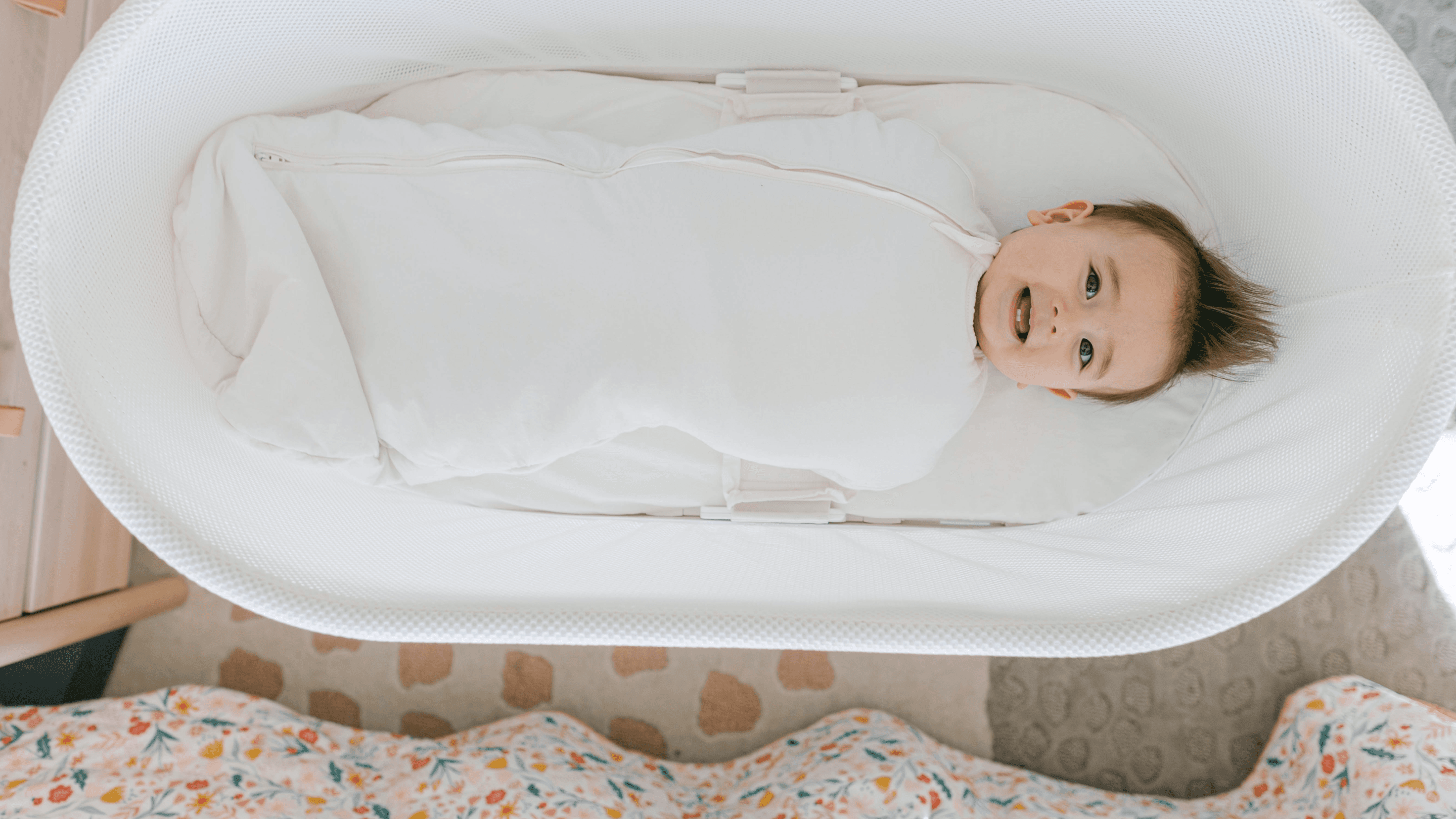 Bebis som ligger i en SNOO insvept i en mysig sovpåse